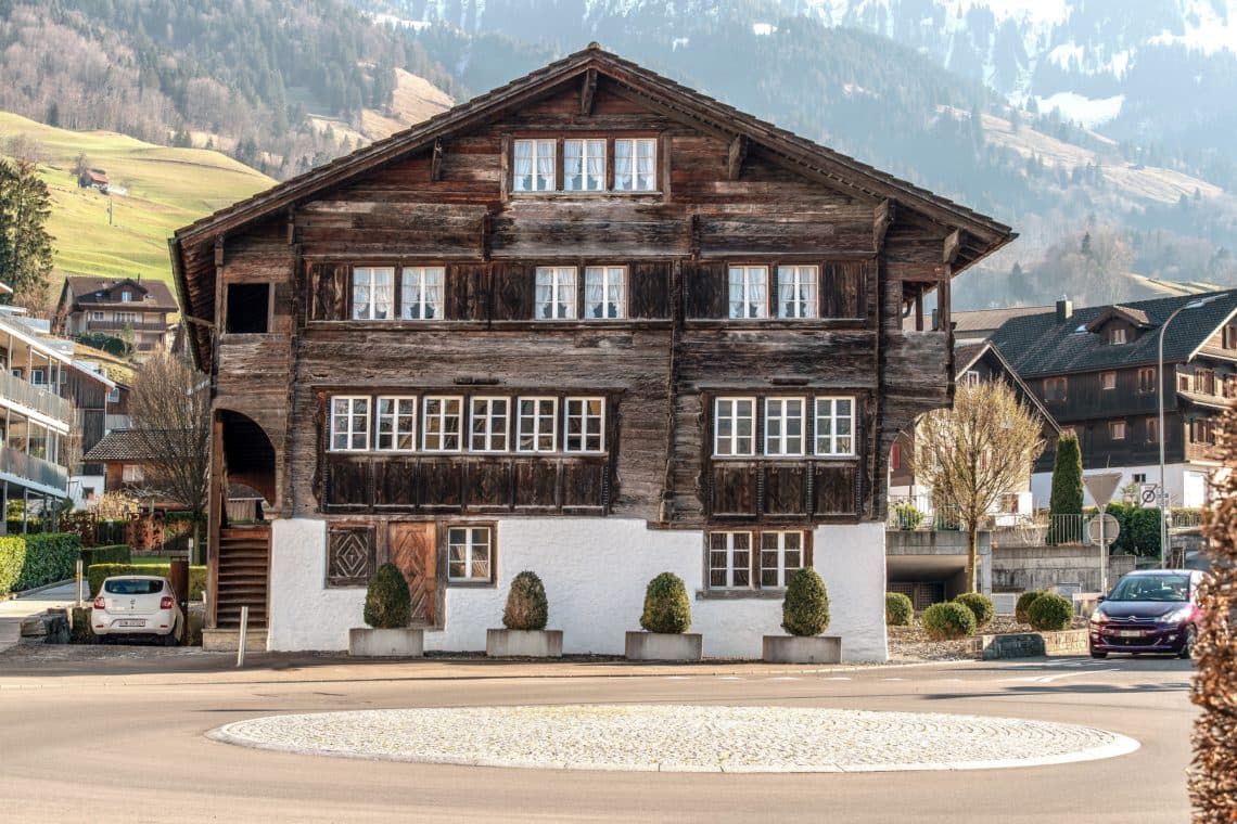 A traditional wooden house in a rural setting with mountains in the background.